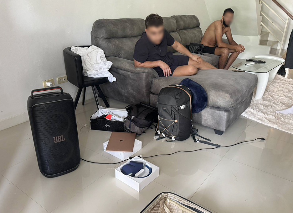 Le suspect français (à gauche) et un autre homme sont assis à l'intérieur de la maison pendant que la police fouille la propriété à la recherche d'objets volés